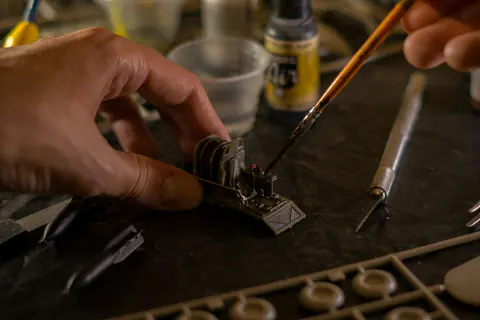 Main peignant une petite maquette avec un pinceau fin